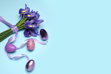 Beautiful iris flowers and painted eggs on light blue background, flat lay. Space for text
