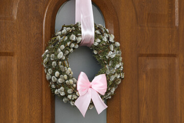 Wreath made of beautiful willow branches and pink bow on wooden door