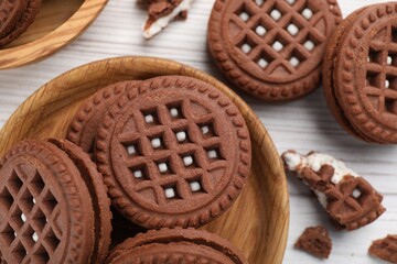 Tasty chocolate sandwich cookies with cream on white wooden table, flat lay