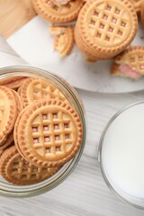Tasty sandwich cookies with cream and glass of milk on white wooden table, flat lay