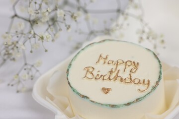 Delicious decorated Birthday cake near dry flowers on white cloth, closeup