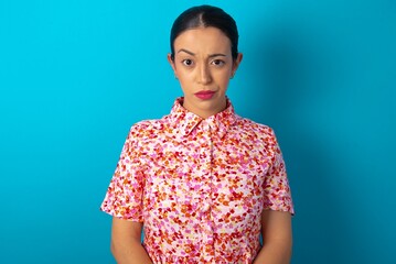 Displeased beautiful woman wearing floral dress over blue studio background frowns face feels unhappy has some problems. Negative emotions and feelings concept