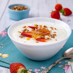 Yogurt with strawberry, honey and granola in a bowl over white wooden table