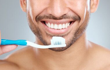 Remember to use a soft bristle brush. a man holding his toothbrush while standing against a grey...