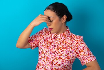 Sad beautiful woman wearing floral dress over blue studio background suffering from headache...