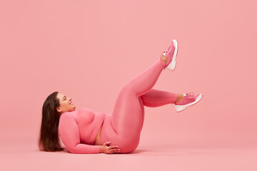 Obraz na płótnie Canvas Motivation. Self-care and well being. Young overweight woman training in sportswear against pink studio background. Concept of sport, body-positivity, weight loss, body and health care