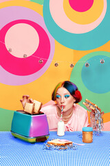 Beautiful young girl with bright makeup and colorful hair drinking milk, eating toast with confetti...