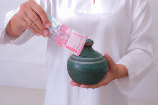 Close-up: A woman's hand slips money into a piggy bank.