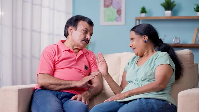 Serious indian senior couple discussing each other on sofa at home - concept of family problem, conversation and relaxation