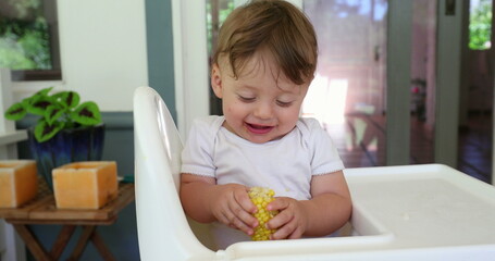 Happy adorable baby on highchair holding healthy corn