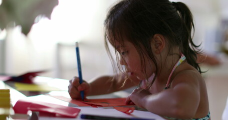 Little girl drawing on paper with blue color pen at home
