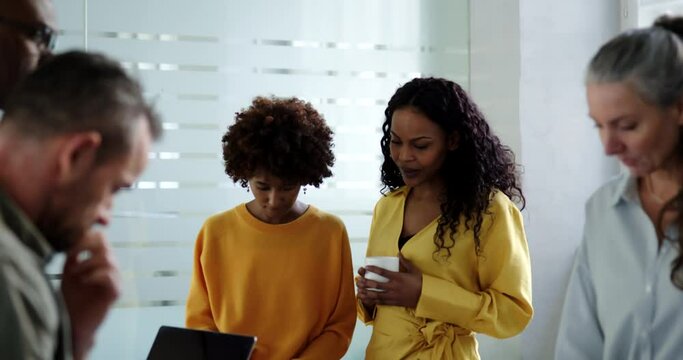 Two smiling young businesswomen discussing a project together during a meeting with coworkers in an office