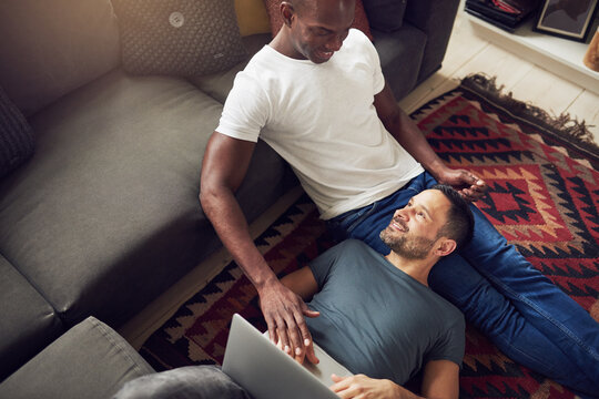 Smiling gentle gay lovers with laptop on floor
