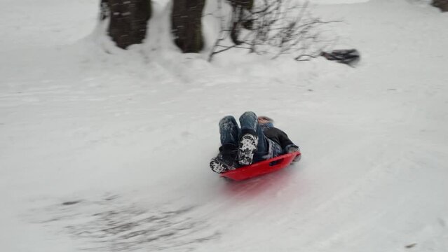 Young boy enjoying the thrill of sliding down a snow-covered hill on his plastic sleds and falling on ice. The perfect depiction of the winter season and the enjoyment children have during their Chris