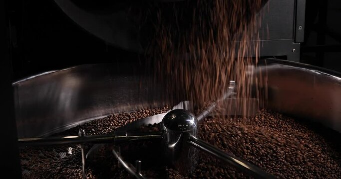 Close-up of the rotating mechanism of a modern coffee roaster stirring the coffee beans. Coffee beans are falling inside. Arabica and robusta coffee production concept.