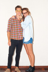 Their relationship is trending. Stylish young hipster couple standing against a white wall while wearing glasses.