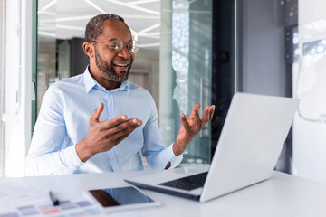 Mature african american boss working inside office with laptop remotely, businessman in shirt on...