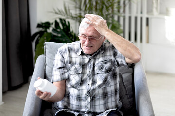 Confused aged man sits on the armchair and holds can with medicine and forgets what to do	