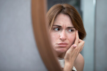 Young beautiful woman looking at mirror and confusing because of new wrinkles	
