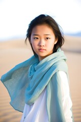Gorgeous young woman with an Asian appearance wearing a blue shawl in the desert. Created with generative A.I. technology.