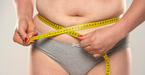 Close up of Woman's fat belly and a measuring tape, isolated on white background.