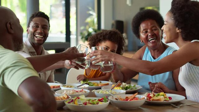 Multi-generation family sitting around table at home doing cheers with water glasses at meal - shot in slow motion