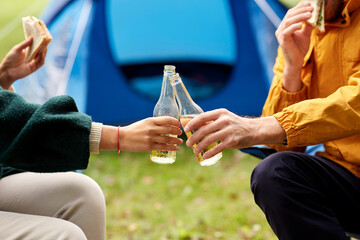 camping, tourism and travel concept - close up of couple drinking beer and eating sandwiches at tent camp