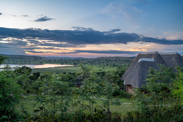 Sunset view of Lake Munyanyange in Uganda, Africa. Colorful sky after a rain storm. Thatched roof...