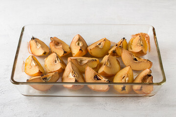Quartered quince baked in a glass form on a light gray background. Stage of cooking vegan pastille or other dessert