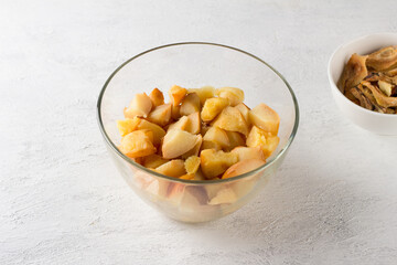 Glass bowl with baked peeled and chopped quince on a light gray background. Stage of preparation of vegan quince pastille or other dessert