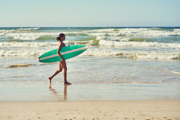 Its time to hit the waves. a young woman out at the beach with her surfboard.