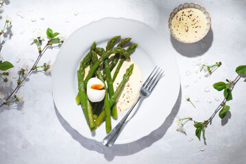 Spring boiled asparagus with egg and hollandaise cheese sauce on a white dish. Spring light lunch, spring mood, summer flowers
