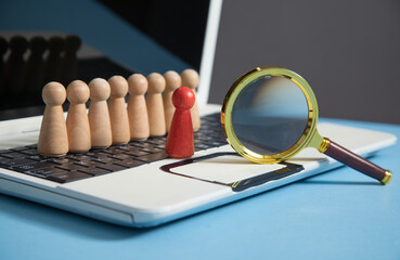 Fototapeta premium Magnifying glass, wooden human figures on laptop keyboard. Candidate selection