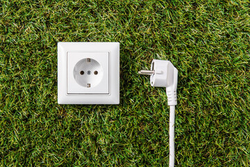 electricity, energy and power consumption concept - close up of socket and plug on green grass background