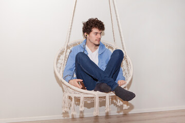 home vacation concept: man sits in rounded hammock having a rest in apartment with wearing blue...