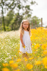 Obraz na płótnie Canvas Girl in a white dress picking flowers in a black eye Susan flower field. Child in a flower meadow at in a patch of yellow and white flowers.