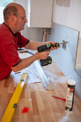 Kitchen Fitters: Mounting the Splashback. A fitter taking care to mount a new metal kitchen splashback into position. From a series of related images.