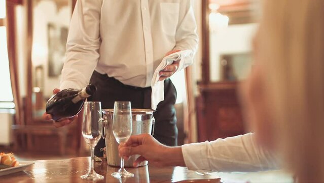 medium static shot of male waiter pouring champagne into two champagne glasses and leaving