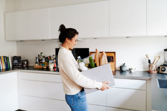 Woman walking with groceries in her kitchen