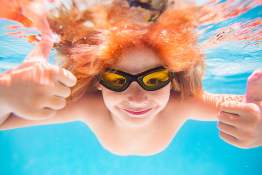 Child swimming underwater with thumbs up. Underwater kid swim under water. Child boy swimming and diving underwater in pool. Summer family summer vacation with children. Underwater kids activity.