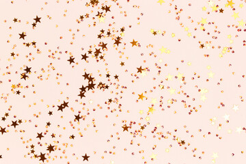 Shiny gold colored stars and crystals confetti on a beige background. Festive texture. Selective focus.