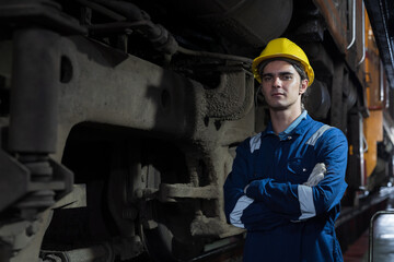 Portrait of male engineer worker standing with crossed arms, wearing safety uniform, helmet and gloves in locomotive garage. Male railway engineer repair locomotive engine in garage