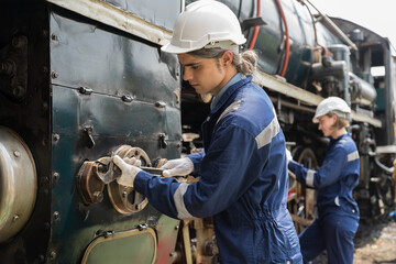 Male and female engineer worker maintenance locomotive engine, wearing safety uniform, helmet and gloves in locomotive garage. Group of railway engineer repair railhead engine in garage