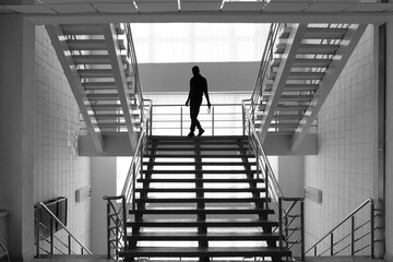 Architecture inside the building. Staircase and a walking person. Steps, steel railings. Up down. Silhouette of a man. Black and white photography