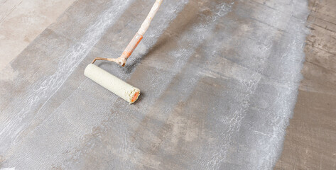 Closeup floor priming process, top view. Worker use primer on concrete floor before leveling,...