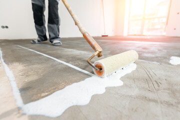 Closeup floor priming process with sun light. Worker use primer on concrete floor before leveling,...