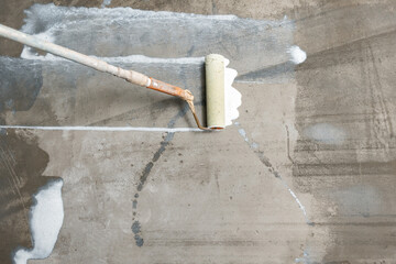 Worker use primer on concrete floor before leveling, strengthening surface. Closeup floor priming...