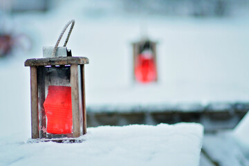 Rustic wooden lanterns on tables outside, red candles inside the lanterns. Tables are covered in...