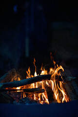 Close-up of a campfire. Fire burning brightly with a big yellow and orange flame in the dark. Firewood and logs burning to ember and ash. Enjoying the warmth of the fire at a cold winter night.