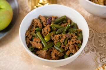 Green beans stewed in spices with meat and garlic on a laid table.